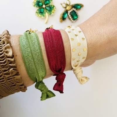 Pulseiras elásticas verde, vermelha e creme com corações dourados e broches verdes em forma de trevo e abelha.