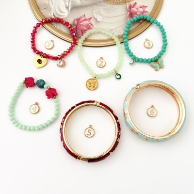 Seis pulseiras coloridas com contas, pingentes e detalhes dourados sobre fundo branco e quadro com flores.