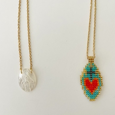 Dois colares com pendentes, um em metal prateado e outro com miçangas coloridas formando um coração