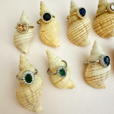 Oito anéis com pedras preciosas coloridas montados em conchas naturais.
