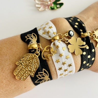 Três pulseiras de tecido elástico preto e branco com estampas e pendentes dourados no pulso.