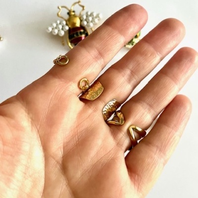 Mão com pequenos pendentes dourados e broche de abelha com pérolas e vermelho ao fundo