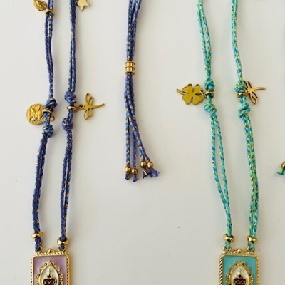 Colares com pendentes retangulares dourados, cordões azuis e verdes, e pequenos amuletos dourados