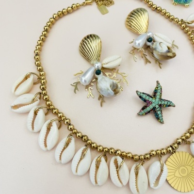 Conjunto de bijuteria com colar de búzios e brincos com elementos dourados sobre fundo rosa