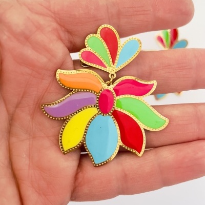 Brinco grande colorido em forma de flor segurado numa mão.