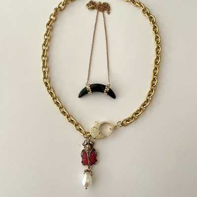 Dois colares dourados, um com pendente de joaninha vermelha e pérola, outro com pendente em forma de lua preta