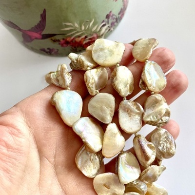 Pérolas iridescentes grandes e irregulares numa mão com fundo floral