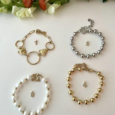 Quatro pulseiras femininas variadas em ouro amarelo, prata e pérolas, numeradas e sobre fundo branco com flores decorativas.