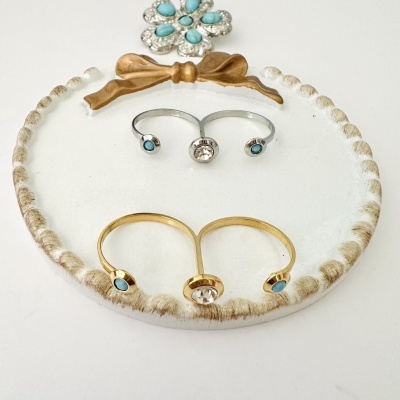 Anéis duplos prateado e dourado com pedras azuis e branca em base decorativa branca com laço castanho