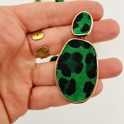 Brinco verde com padrão animal print e moldura dourada segurado na mão
