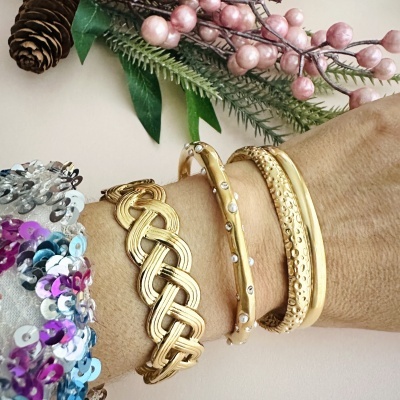 Pulseiras douradas com diferentes texturas e padrões num pulso com fundo natural