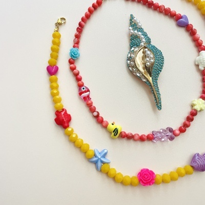 Colar e pulseira de contas coloridas com motivos variados e um broche decorativo azul com pérolas e strass