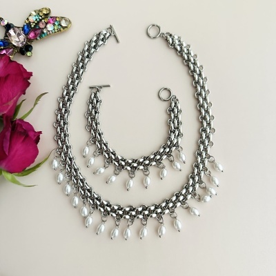 Conjunto de bijuteria prateada com pérolas e flores rosadas ao lado
