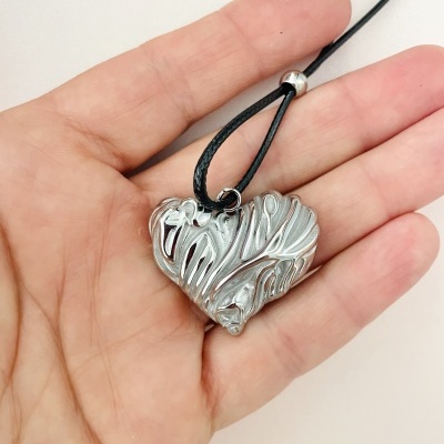 Colar com pendente de coração prateado texturizado suspenso em cordão preto na mão