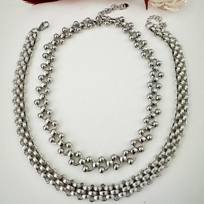 Dois colares prateados em fundo branco com pássaro vermelho e flor branca ao lado