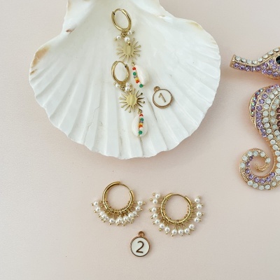 Dois pares de brincos dourados com contas e pérolas sobre concha branca