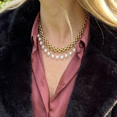 Colar dourado com pérolas em pessoa com camisa rosa e casaco preto