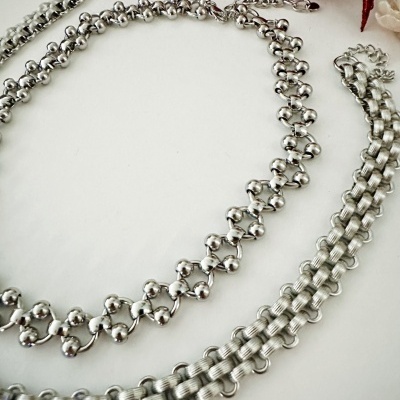 Colares prateados com texturas variadas sobre fundo branco e objeto vermelho