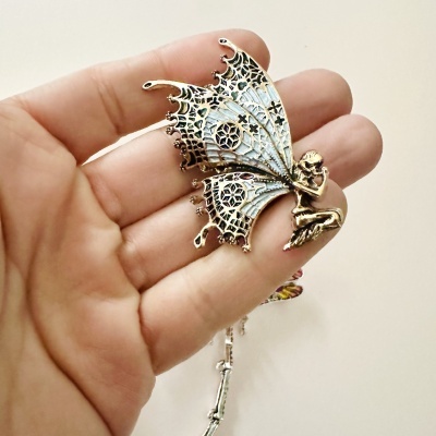 Broche dourado de fada com asas em padrão de renda, na mão