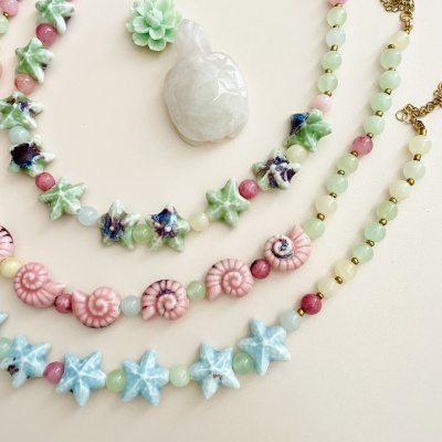 Colares com contas coloridas em formas de estrelas, conchas e flores em fundo claro