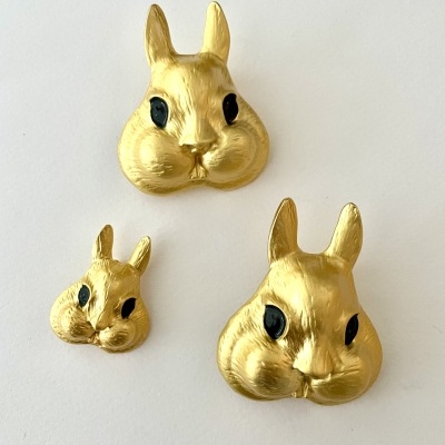 Três cabeças de coelho douradas com olhos pretos em fundo branco