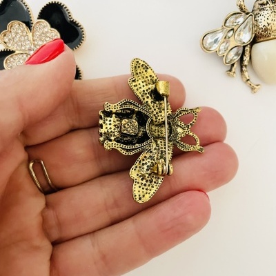 Broche abelha dourada com alfinete segurado por mão em fundo branco