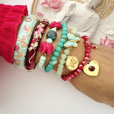 Conjunto de pulseiras coloridas com contas e detalhes dourados num pulso com mangas vermelhas.