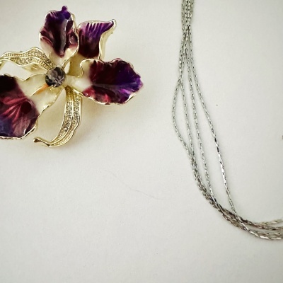 Colar com pendente de flor roxa e branca com detalhes dourados e pedrinhas brilhantes