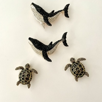 Broches de tubarões preto e prateado e tartarugas preto e dourado sobre fundo branco.