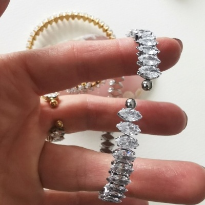 Pulseira metálica com pedras brilhantes em formato losango e uma joia de abelha colorida ao fundo