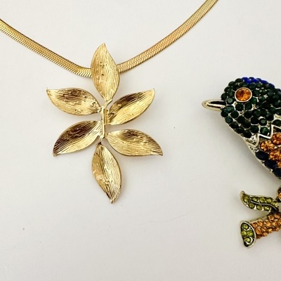 Colar com pendente dourado em forma de folhas e broche de ave colorido