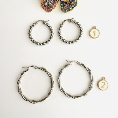 Dois pares de brincos de argola prateados, dois medalhões numerados e um broche colorido com pérola.