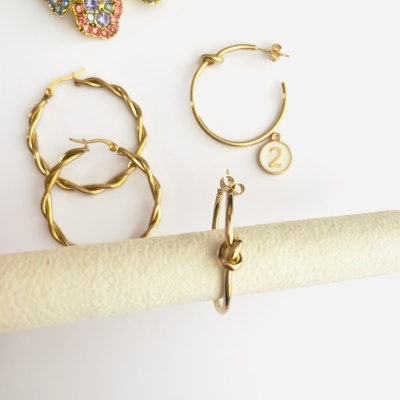 Brincos em metal dourado com diferentes designs e broche floral colorido com pérola no fundo.