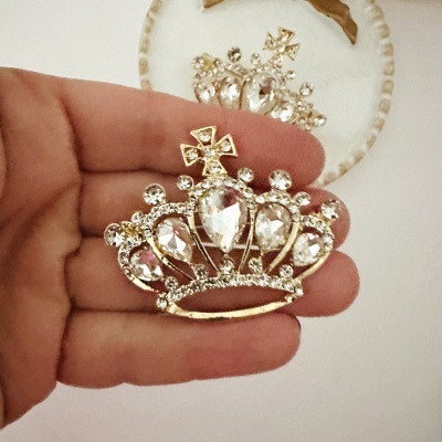 Broche de coroa dourada com pedras brilhantes segurado por mão em frente a espelho.