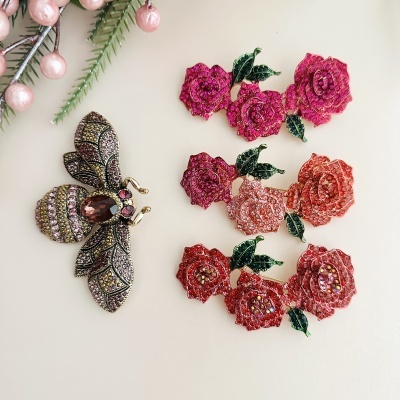 Brincos florais rosa, coral e vermelho e broche de abelha com pedras brilhantes sobre fundo branco