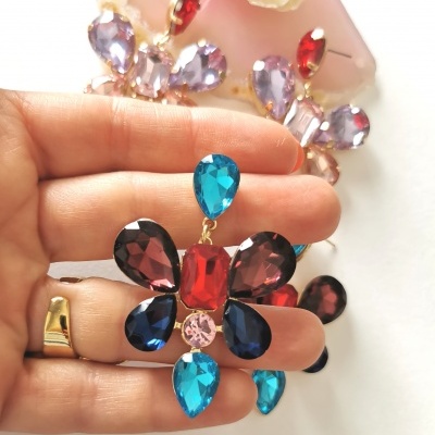 Brincos florais coloridos segurados por mão com fundo branco.