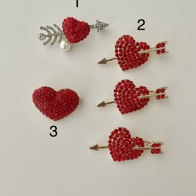 Broches em forma de coração vermelho com detalhes em branco e prateado sobre fundo branco