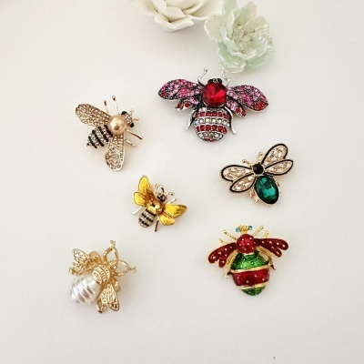 Broches de abelhas com pedras coloridas sobre fundo branco e flores cerâmicas