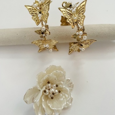 Brincos dourados com borboletas e pérolas e broche branco em forma de flor com pérolas