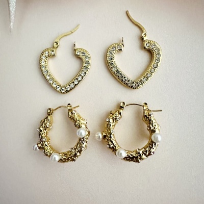 Dois pares de brincos de argola dourados, um com pedras em forma de coração e outro com textura irregular e pérolas falsas.