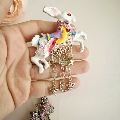 Broche coelho branco com cristais rosa e pendentes dourados em forma de estrelas e lua.