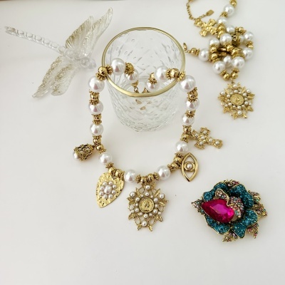 Pulseira e colar de pérolas e ouro com pendentes, broche colorido e figura decorativa em cristal, tudo sobre fundo branco.