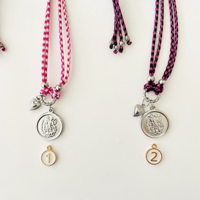 Colares com medalhões prateados e cordões rosa e preto, em fundo branco