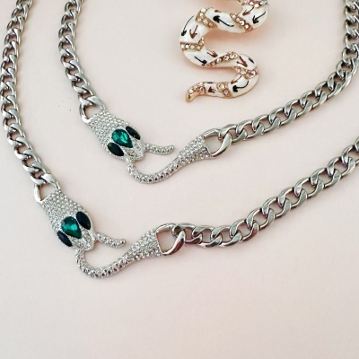 Colar de corrente como cobra prateada com olhos verdes e anel decorativo dourado com padrões