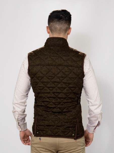 Colete castanho matelassê visto de costas, em modelo masculino com camisa xadrez clara e calças cáqui.