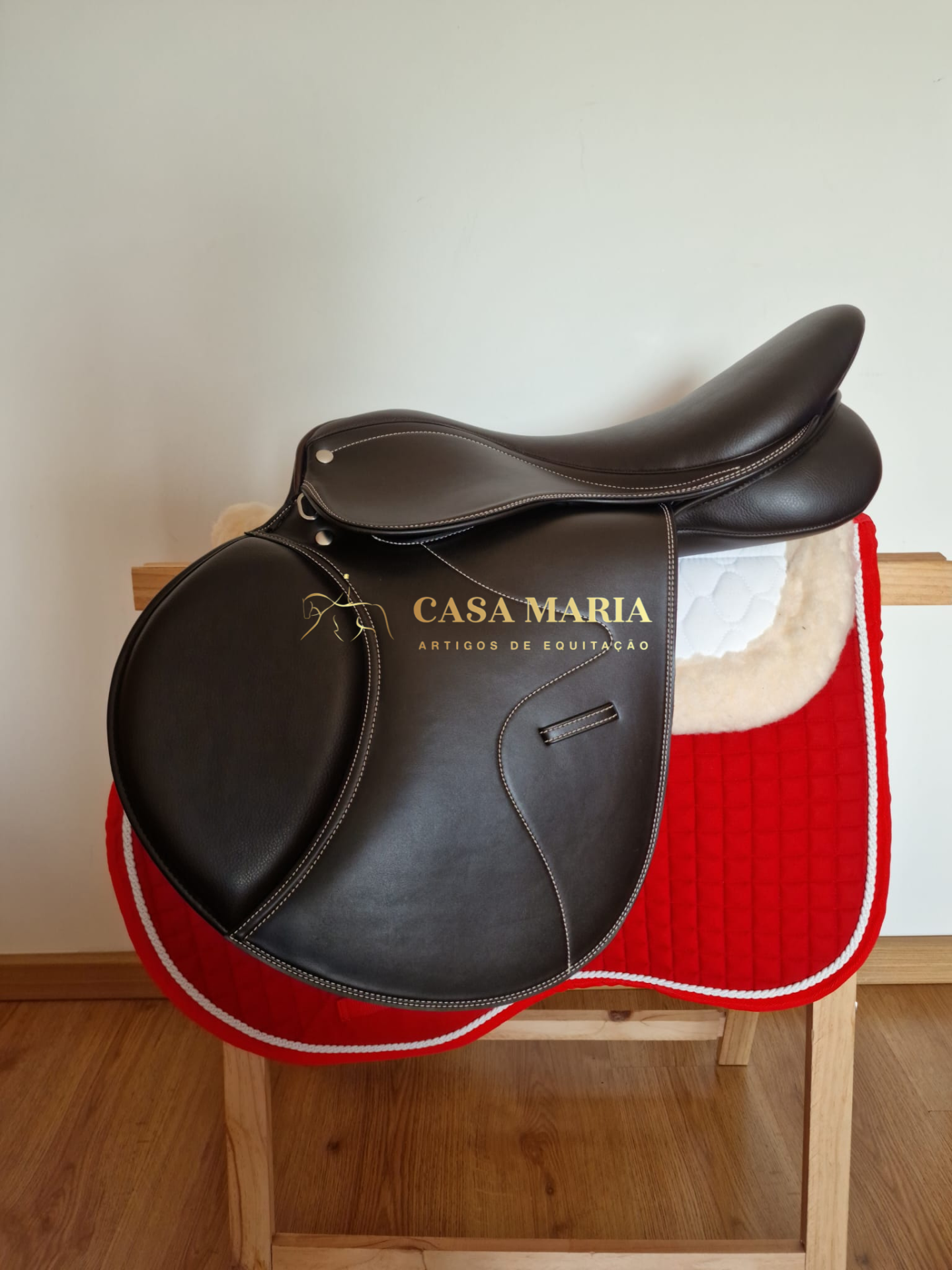 Sela negra de couro sobre manta branca e vermelha num suporte de madeira