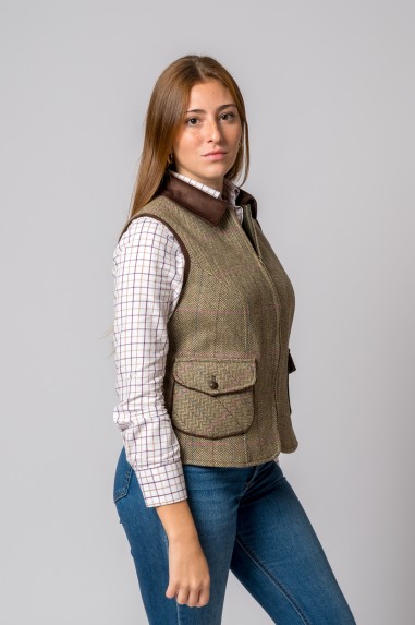 Mulher a usar colete verde tweed com bolsos e botão, camisa branca xadrez e calças de ganga azul.