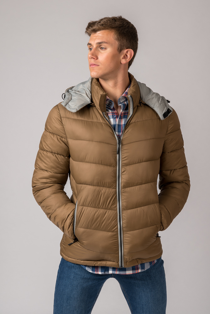 Homem com casaco acolchoado bege, capuz cinzento, camisa xadrez e jeans azuis