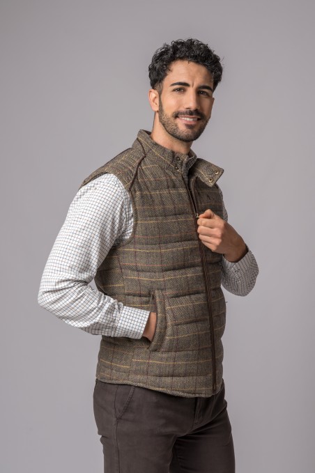 Homem com colete acolchoado castanho xadrez e camisa branca de manga comprida frente cinzenta
