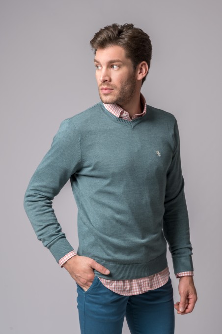 Homem com camisola verde-azulada, camisa xadrez rosa e branco e calças azul-acinzentadas